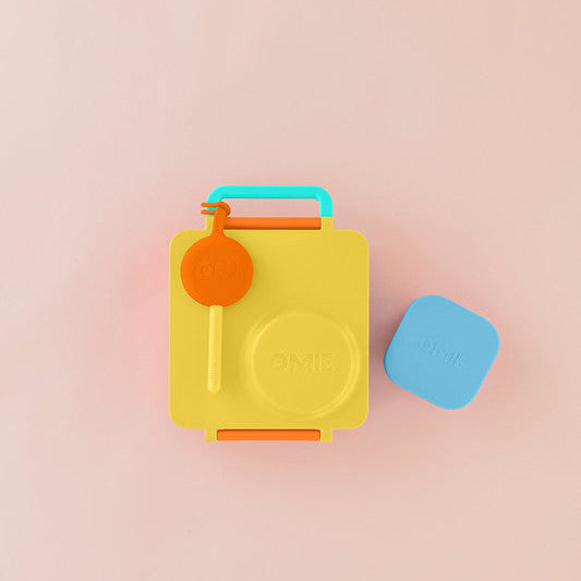 Yellow lunch box with orange handle and blue lid on a pink background