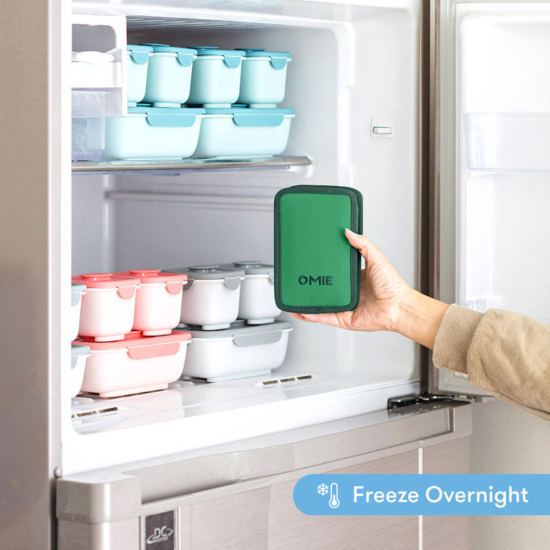 Green OMIE product held in front of a refrigerator with food containers.