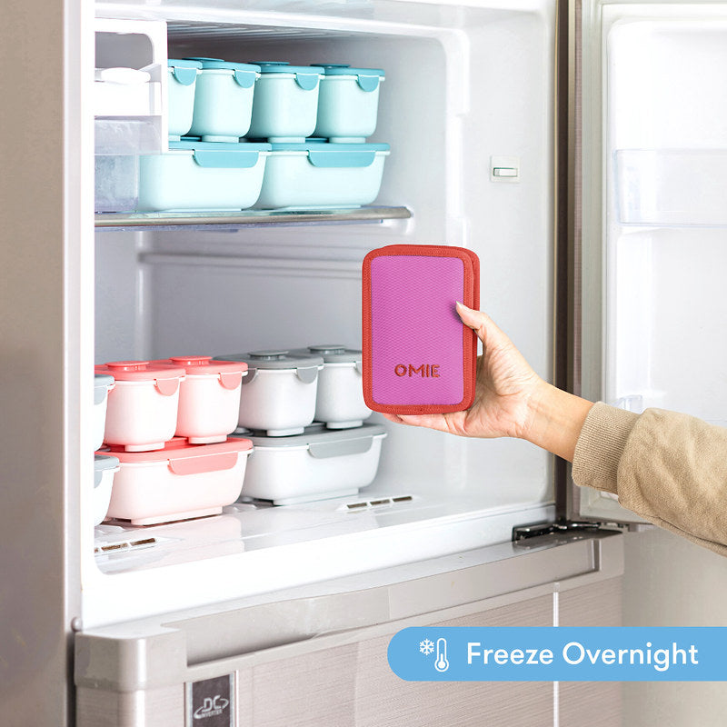 Person holding a pink silicone container labeled 'OMIE' in front of an open refrigerator with other containers.