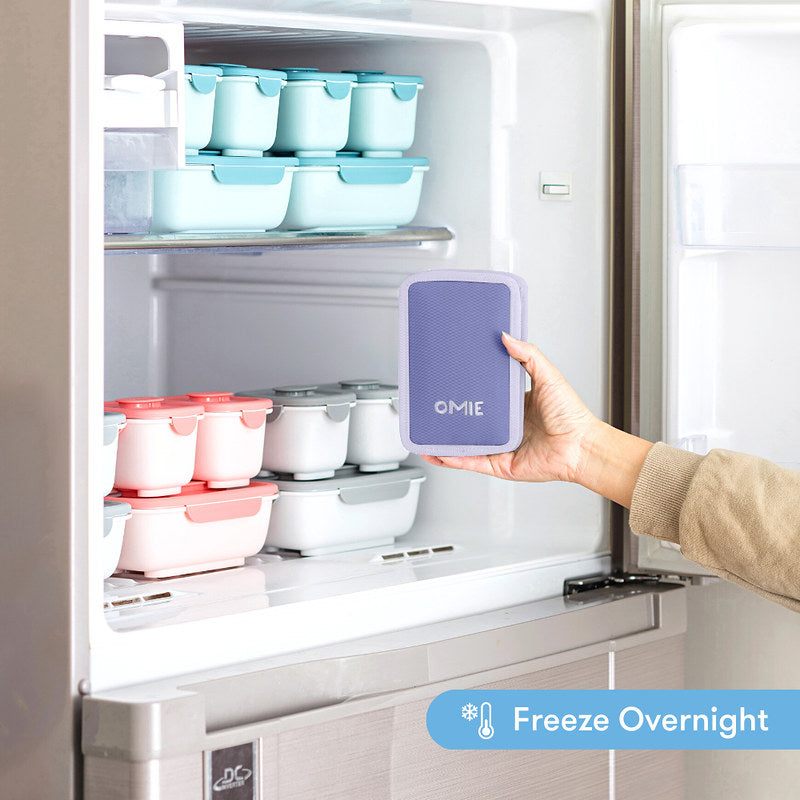 Hand holding a purple OMIE product in front of a refrigerator with food containers.