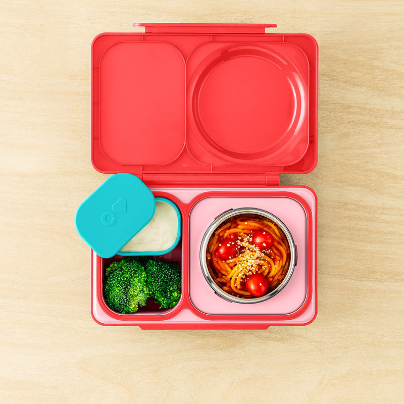 Pink bento box with compartments containing food on a wooden surface
