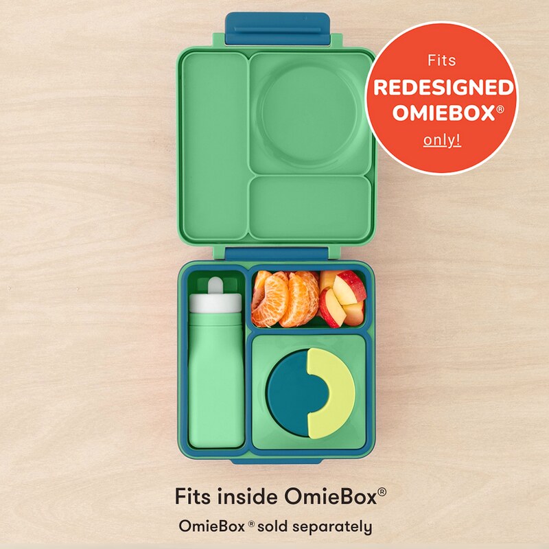 Green bento box with compartments containing food and a bottle, on a beige background.