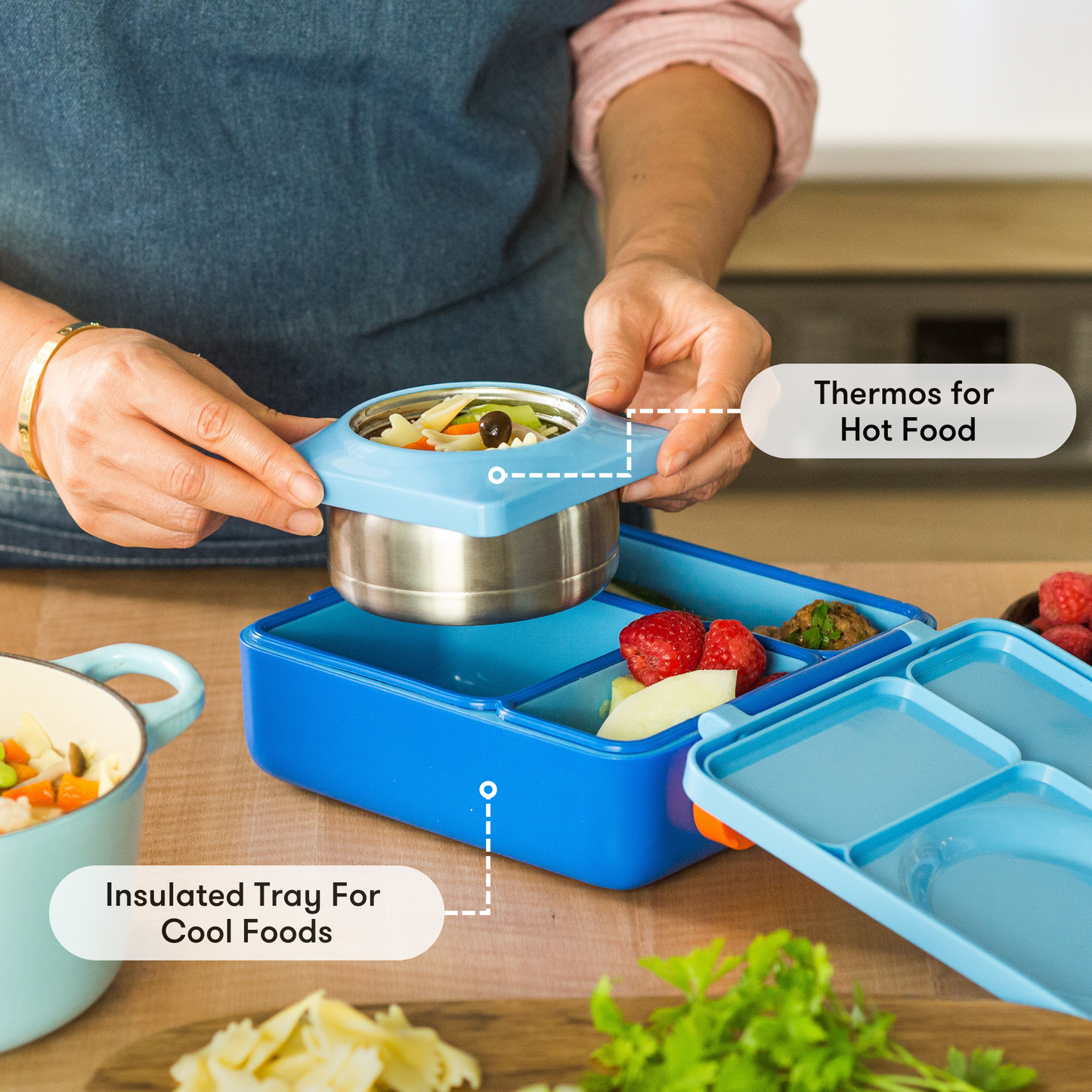 Person using a blue lunch box with a thermos and insulated tray to store hot food.