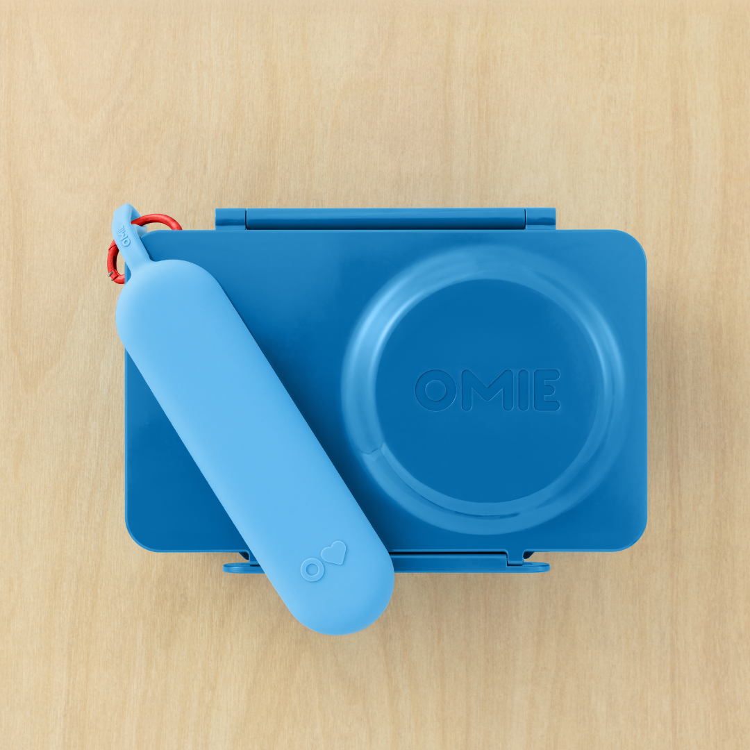 Blue container with a lid and handle on a wooden surface, featuring the brand 'OMIE'.