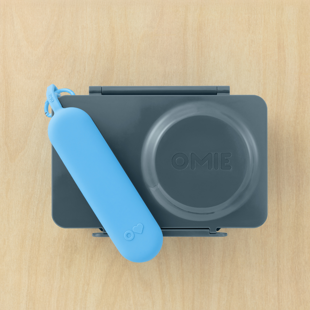 Gray container with blue handle on a wooden surface, featuring the brand 'OMIE'.