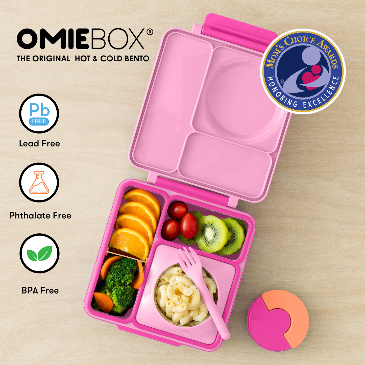 Pink bento box with compartments filled with food on a beige background, featuring OmieBox branding and safety certifications.