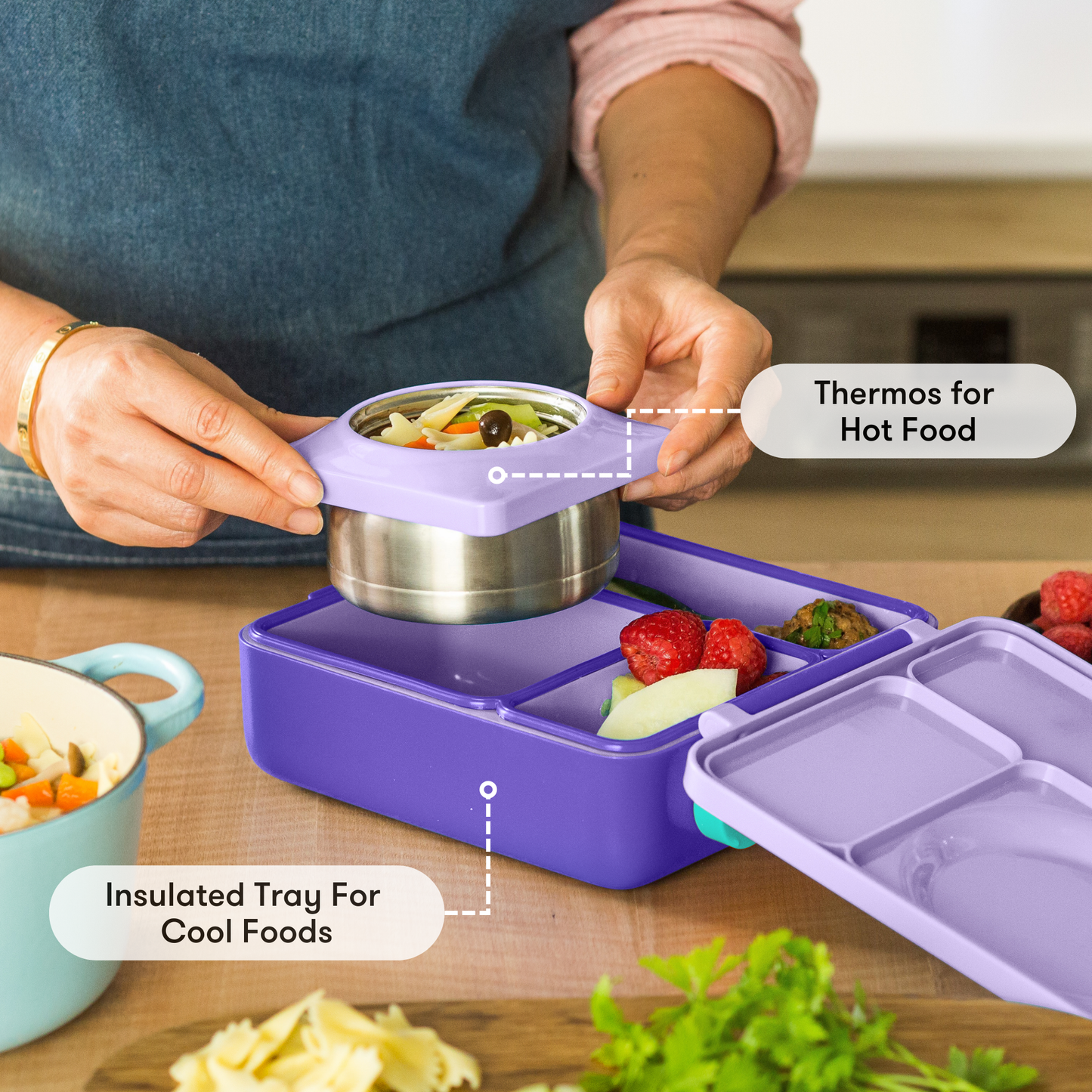 Person using a purple thermos and insulated tray with food on a wooden table.
