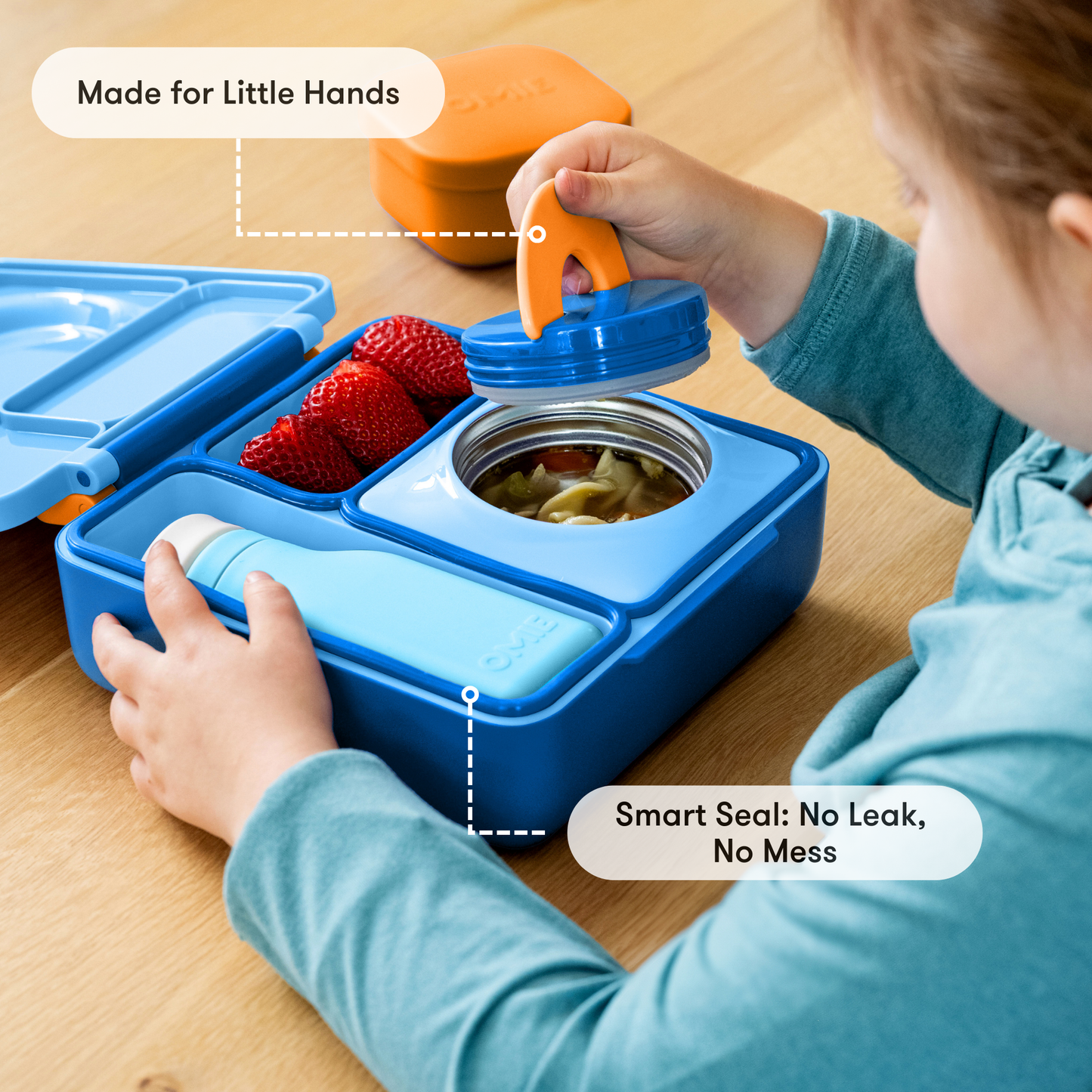 Child interacting with a blue bento box on a wooden surface, with text highlighting features like 'Made for Little Hands' and 'Smart Seal: No Leak, No Mess'.