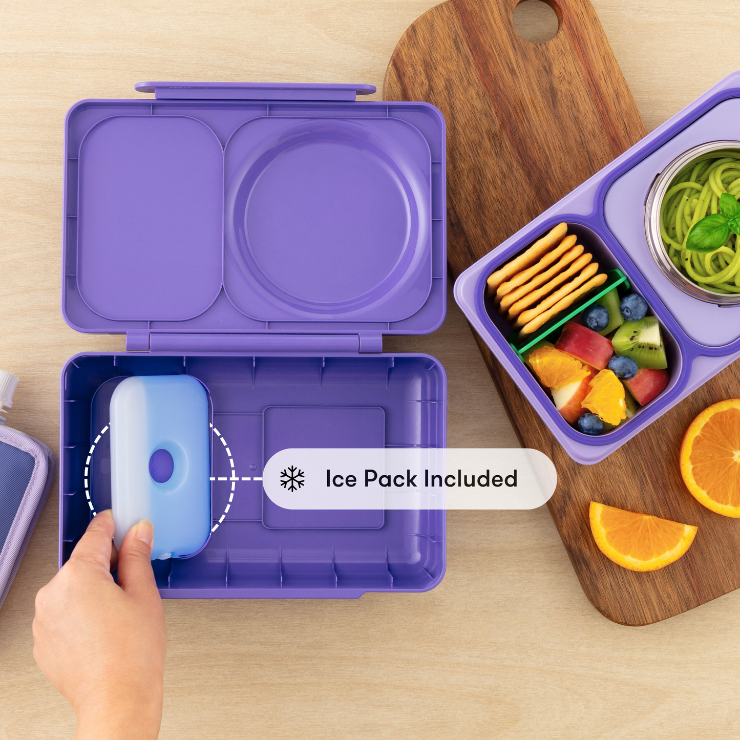 Purple bento box with ice pack included, next to a lunchbox with snacks on a wooden surface.