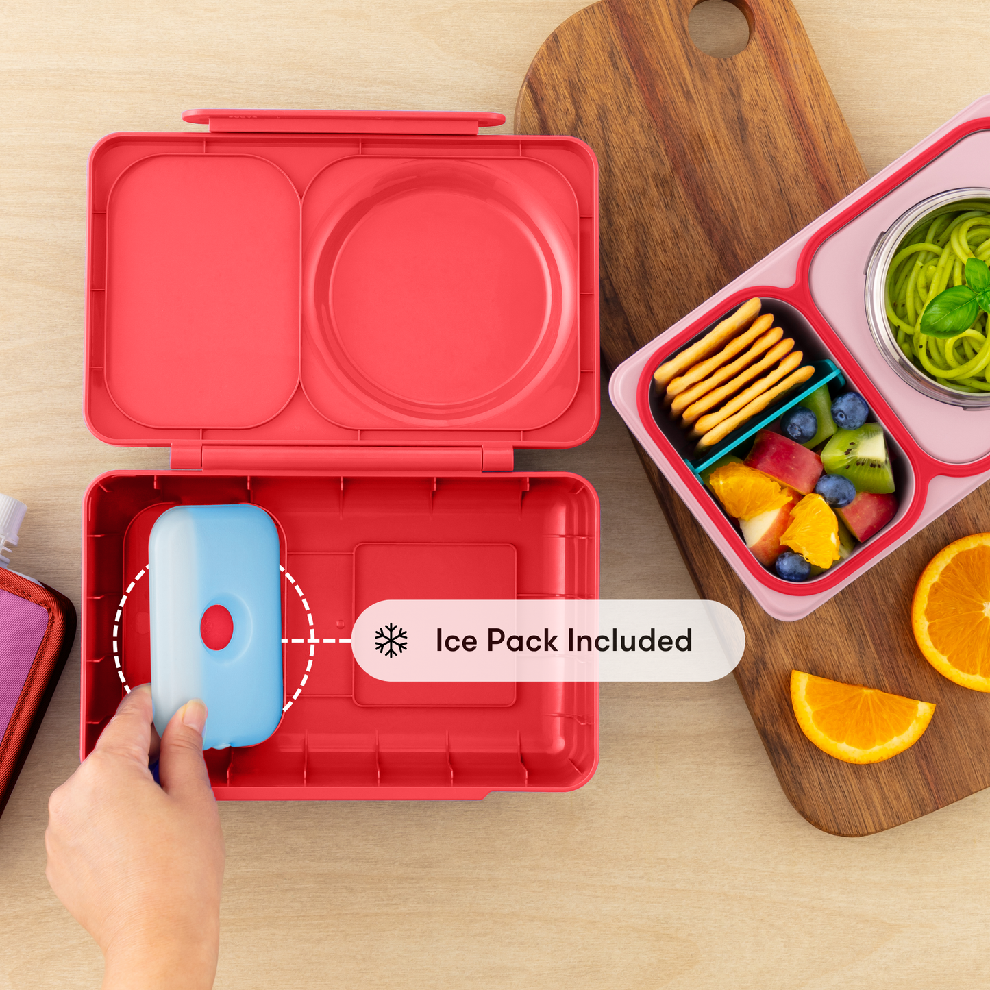 Red bento box with ice pack included, next to a colorful snack container on a wooden surface.