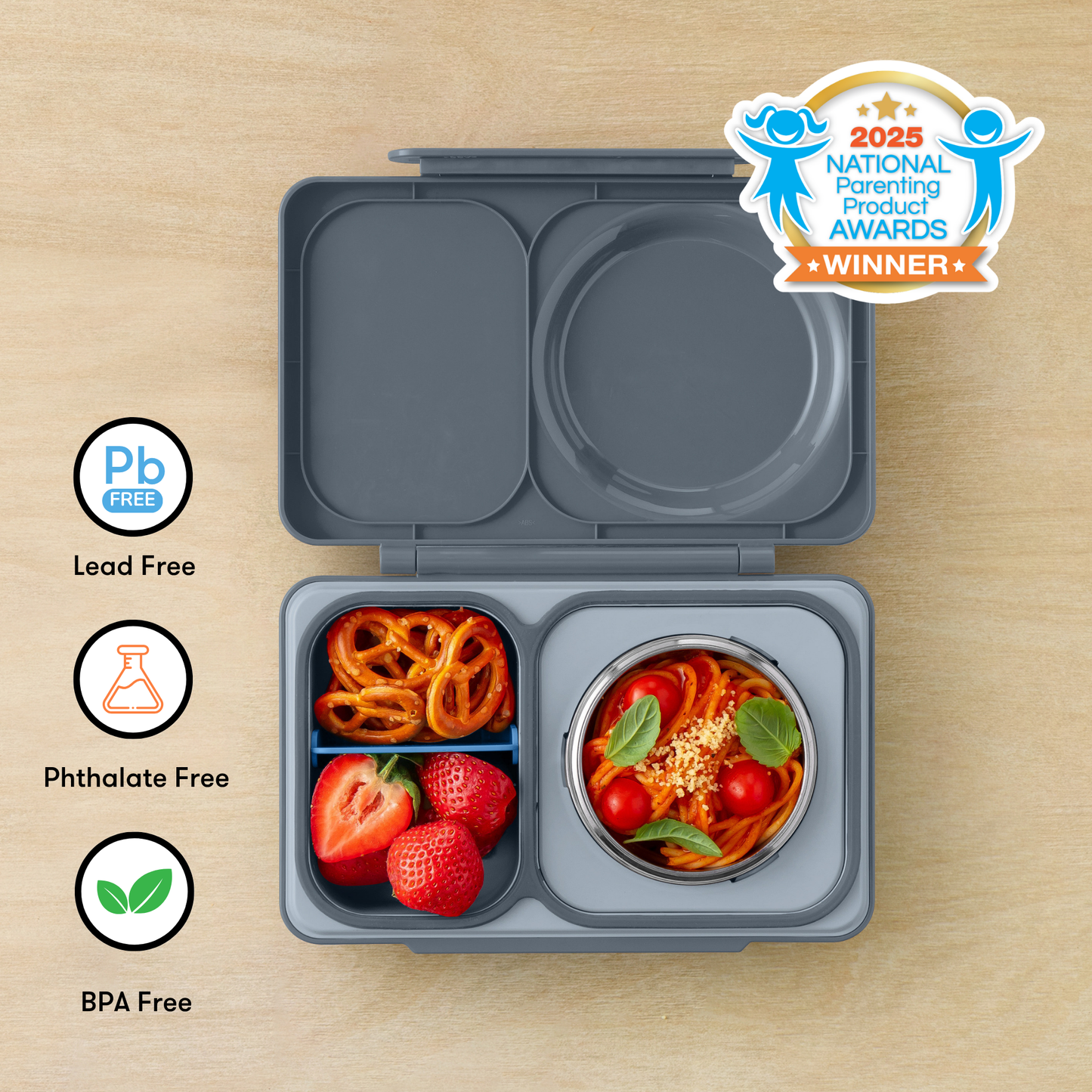 Gray bento box with compartments containing food items on a wooden surface, featuring 'Pb Free', 'Phthalate Free', and 'BPA Free' labels, and a 2025 National Parenting Product Award winner badge.