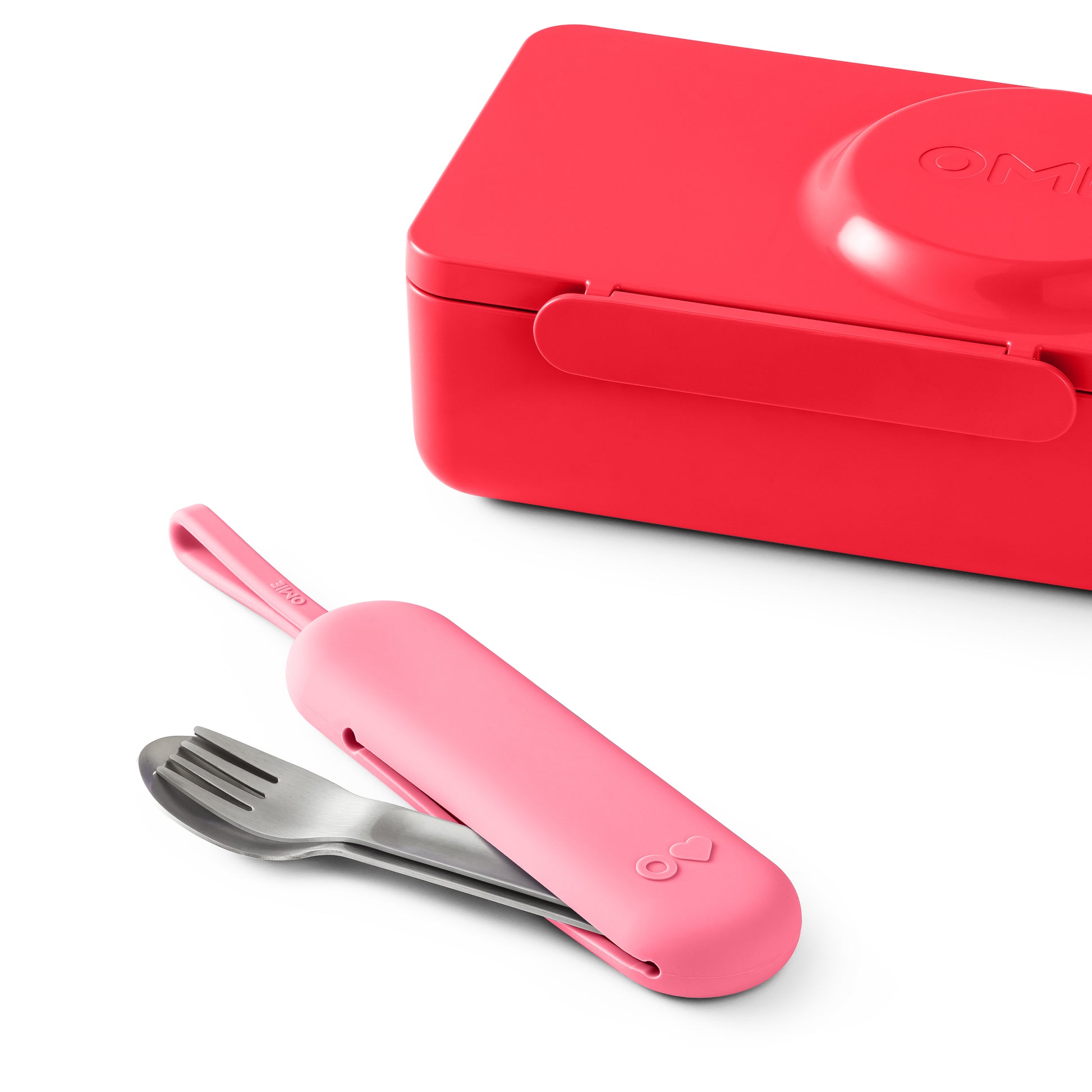 Pink fork and spoon set with case next to a red lunch box on a white background