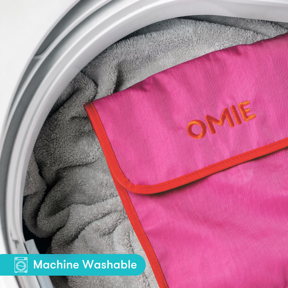 Pink towel with 'OMIE' branding inside a washing machine.