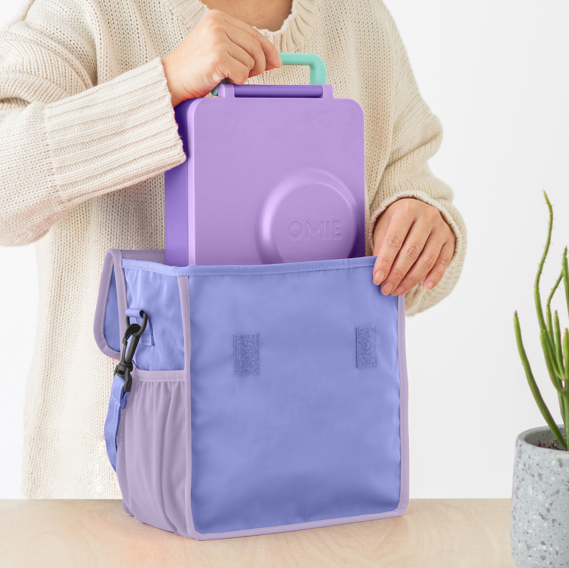 Person holding a purple bag with a smaller purple container inside, on a light background.