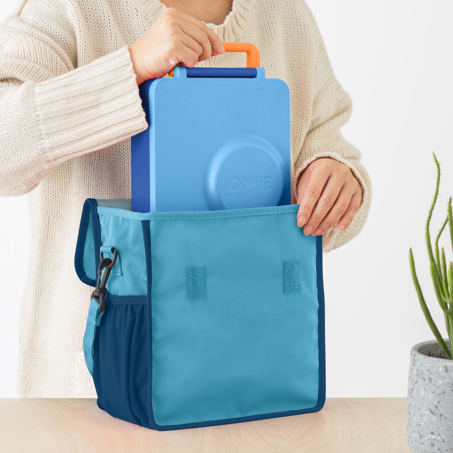 Person holding a blue cooler bag with an orange handle against a neutral background