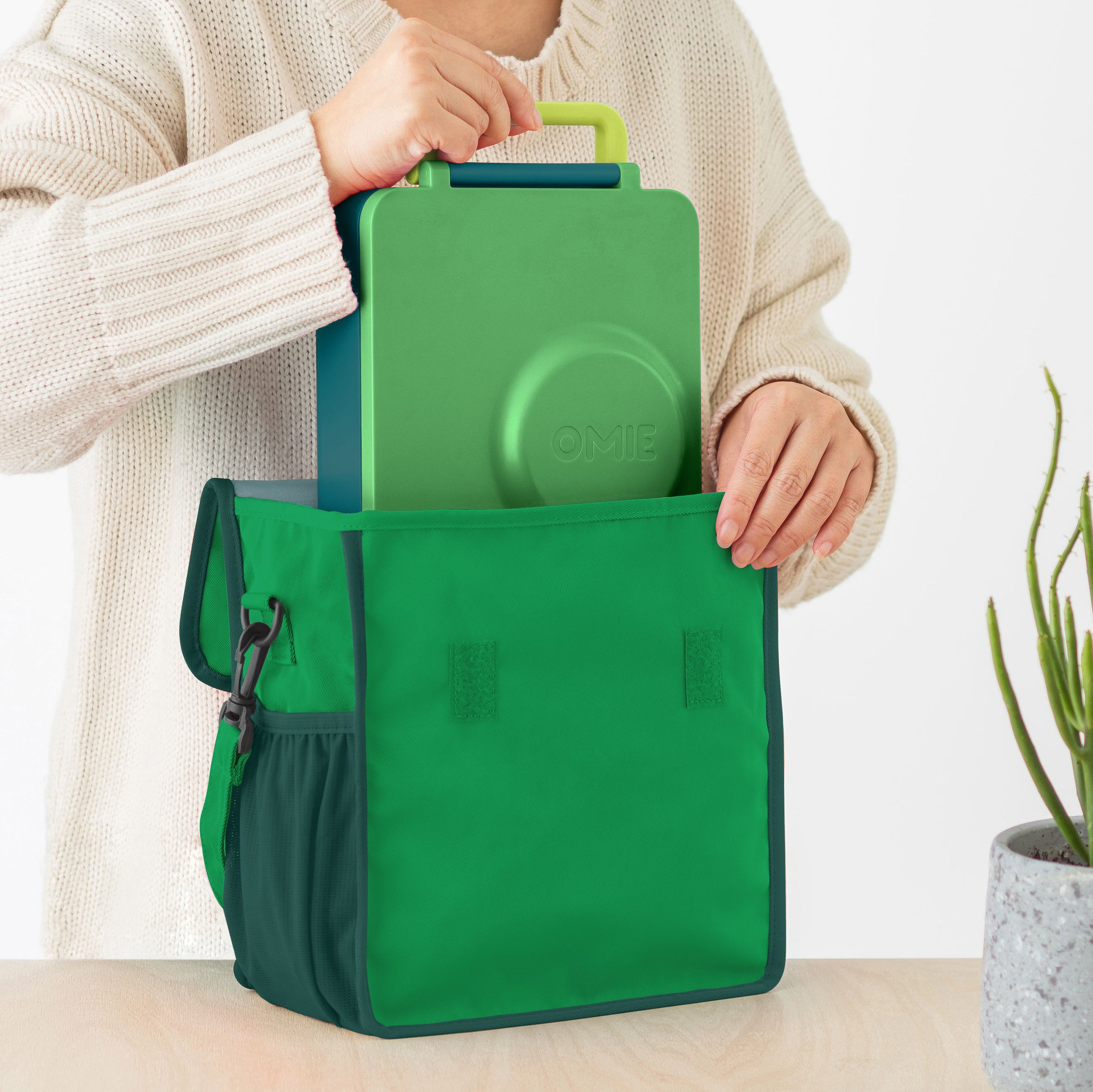 Green lunch bag with a smaller green container held by a person against a neutral background