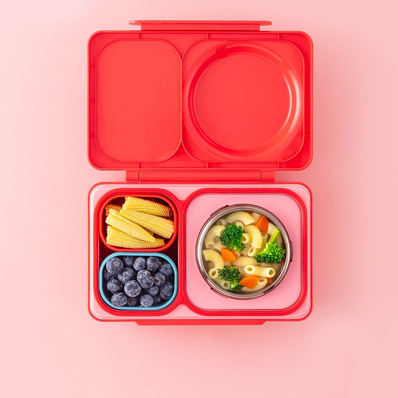 Pink bento box with compartments containing food on a pink background