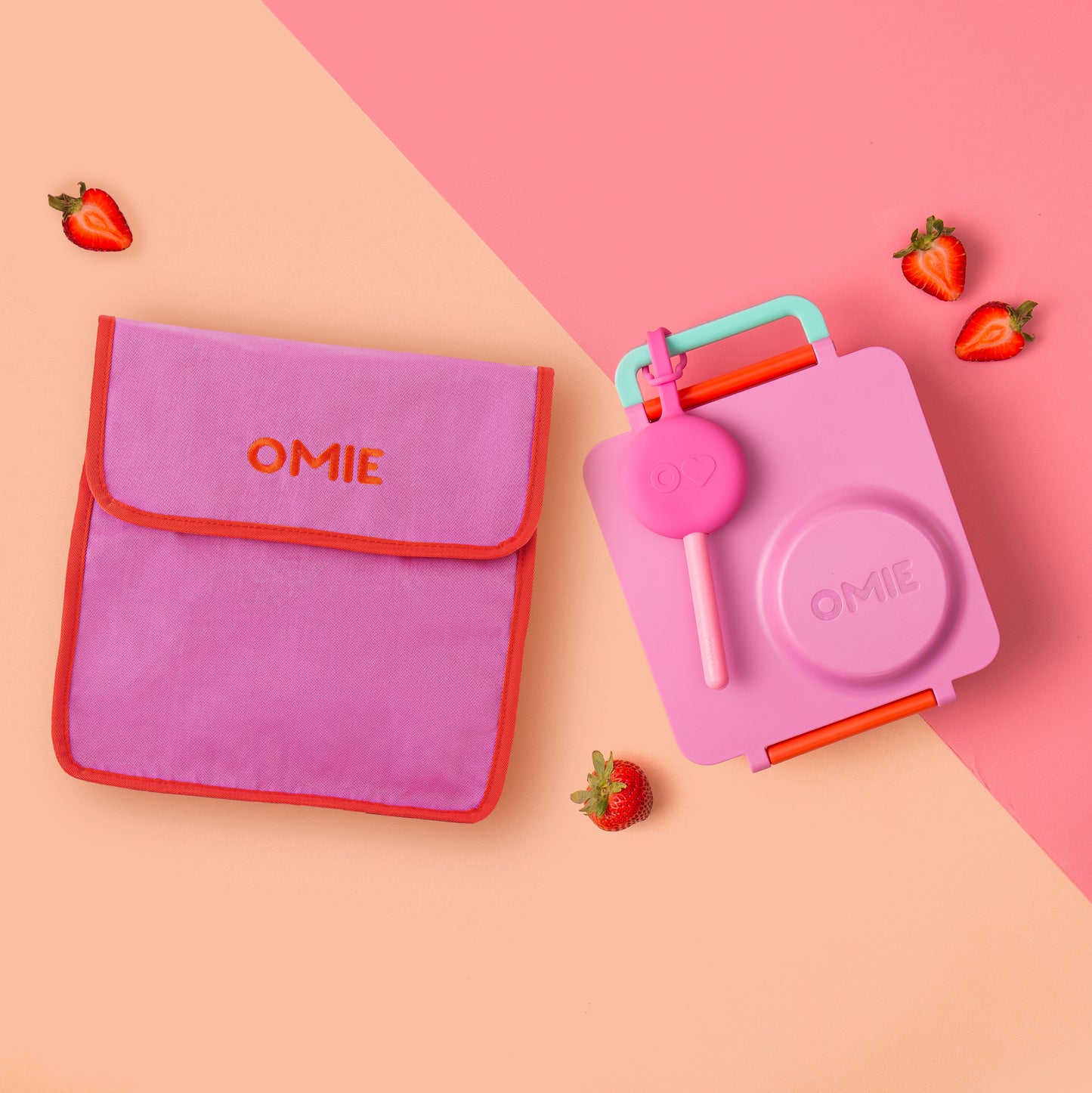 Pink and red OMIE lunch bag and container on a pink and beige background with strawberries.
