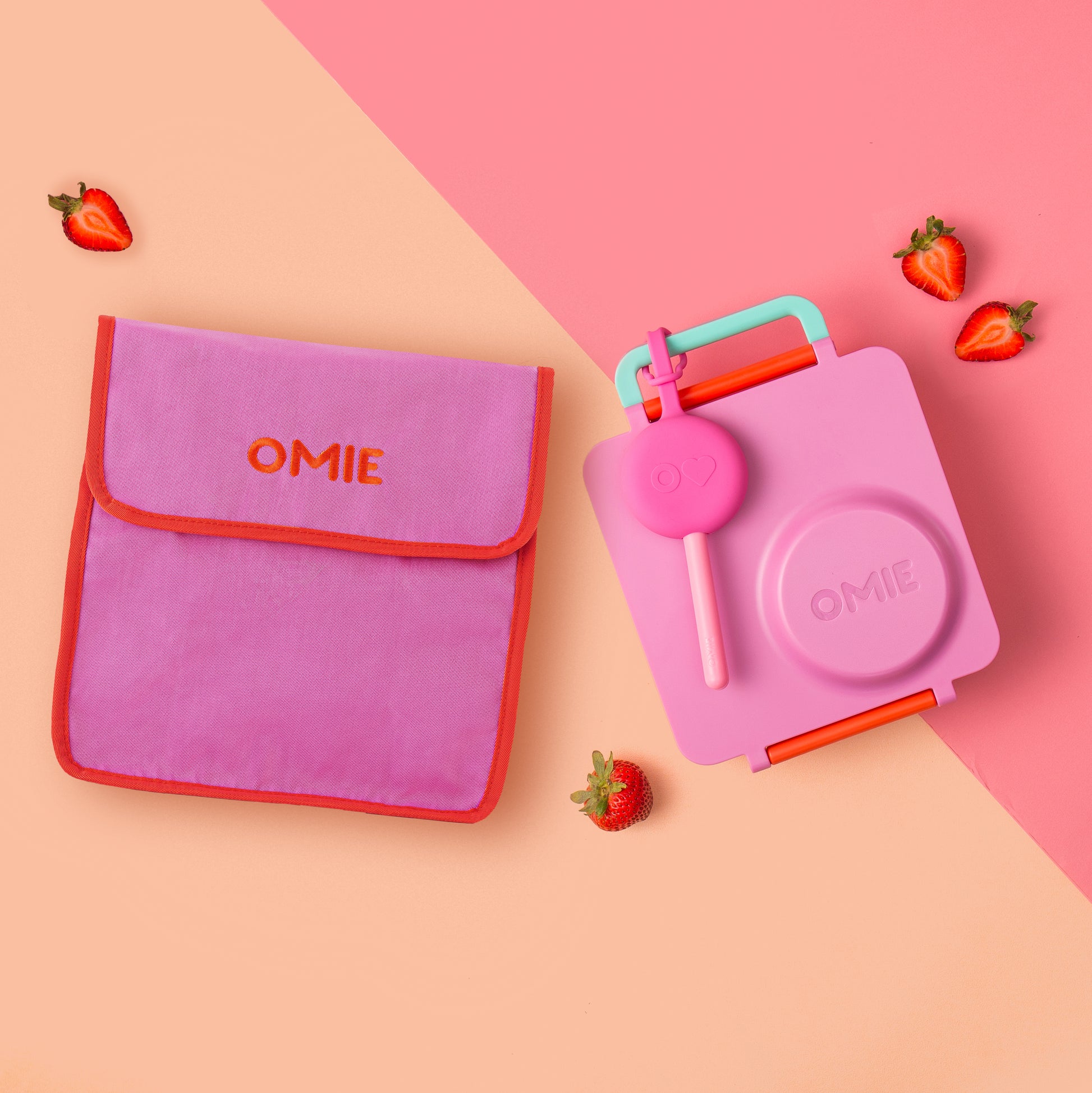 Pink and red OMIE lunch bag and container on a pink and beige background with strawberries.