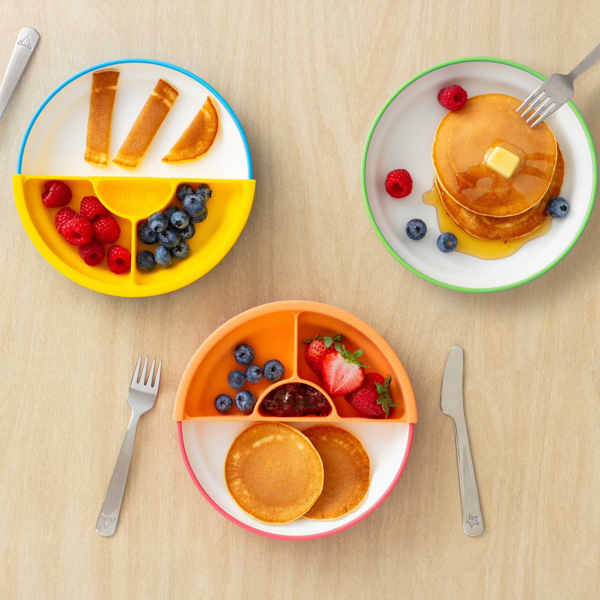 Three children's plates with food on a wooden table